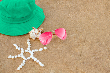 Fototapeta na wymiar Bright green hat, pink glasses, unusual shell, sun laid out with small white pebbles on sand beach, copy space. Concept summer beach holiday in hot countries, summer holidays. Blank packaging layout.