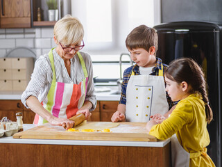 Grandmother and her grandchildren making cakes together in the home kitchen. Children helping...