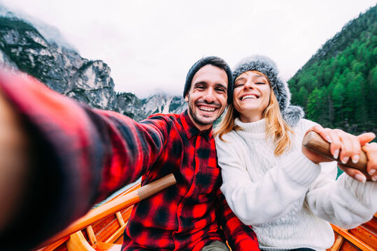 Romantic couple of adults in love taking selfie on a boat visiting an alpine lake at Braies, Italy - Couple, technology, travel and happy lifestyle concept - Cold colours.