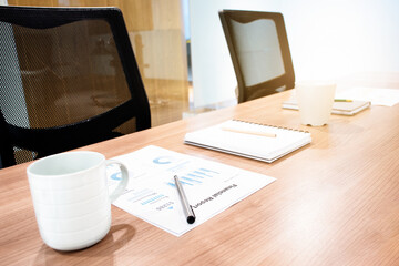 Fototapeta premium Coffee cup ,paperwork and notebook on table with two black armchairs in meeting room