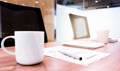 Coffee cup ,paperwork and notebook on table with two black armchairs in meeting room
