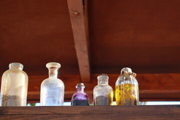 Dusty glass jars of potions. Old small jars are on a wooden shelf.