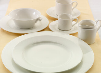 Fototapeta na wymiar Vajilla de porcelana blanca sobre mantel Amarillo. White porcelain tableware on a yellow tablecloth.