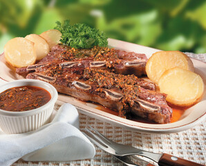 Costillar en salsa con patatas asadas y salsa picante. Ribs in sauce with roasted potatoes and hot sauce.