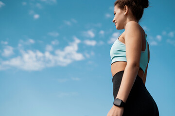 A woman does sports on the street. Fitness and a healthy lifestyle. The coach takes a break between exercises. Uses a smart watch to measure the pulse on the hands.
