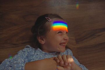 girl lies with her eyes closed and a glare of a rainbow on her face