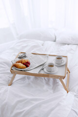 Decorative flowers near white bed for young couple with wooden tray and breakfast