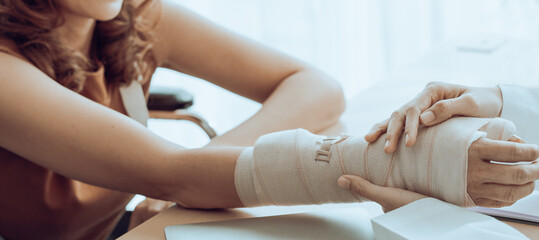 Close up of orthopedic doctor investigates woman patient broken arm covers with a splint plaster cast. Trauma can happen after people fall and are hurt physically by accidents. Rehab center services. - obrazy, fototapety, plakaty