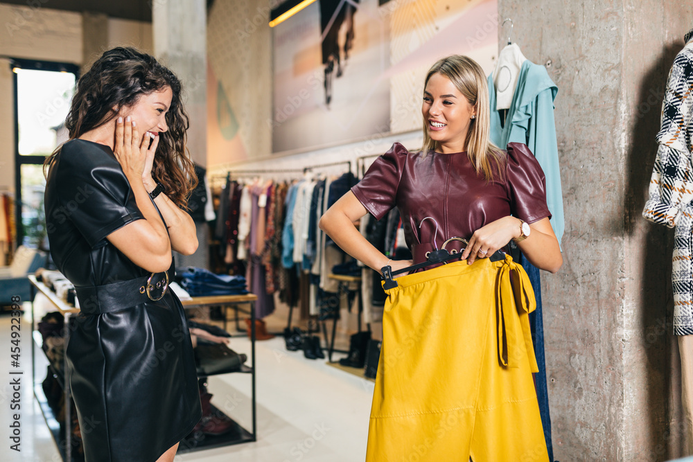 Wall mural Beautiful young women trying elegant clothes in expensive boutique or store..