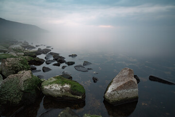 Rocks and stones covered with green algae. Smooth clear water.