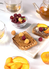 Healthy breakfast. Sandwiches or toasts with peanut butter, chocolate paste and yellow and red raspberries, blackberry on white table