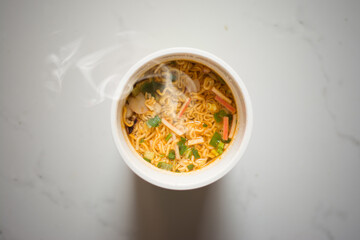 Hand to pickup tasty noodles cup with smoke in bowl selective focus. Asian meal on a table, junk...