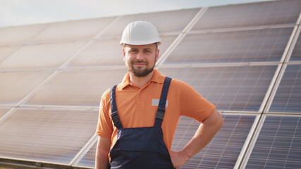 Portrait of confident engineer of solar cell farm industry. Staff confident pose Solar cell panel installation. Close up portrait of male worker in protective helmet standing near solar panel