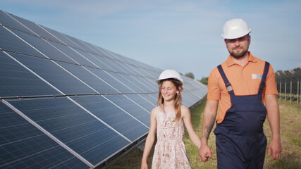 A father working in a solar power plant tells his daughter about his work, shows green energy,...