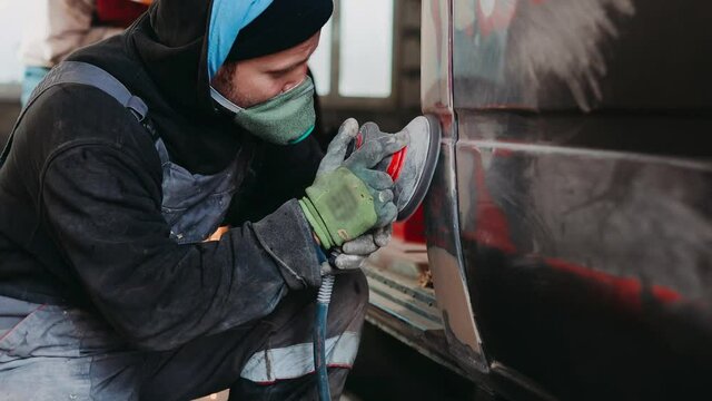 man master grinds a putty on a car body with a polishing machine, restoration of a car body.