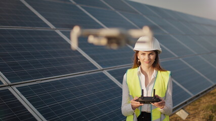 Engineer woman in hardhat holding tablet computer operating flying drone in solar plant....