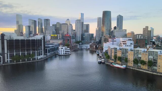 Panoramic view of Canary Wharf business hub. Landing shot over water surface. Group of tall skyscrapers in modern commercial district. London, UK