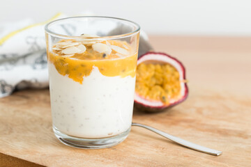 Glass of yogurt with passion fruit on top, served on a wooden table.