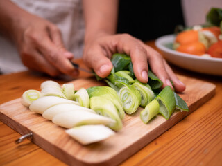 Female hand using kitchen knife to cut Japanese Long Onion or Japanese Scallion or Green Onion on wooden cutting board. Woman is preparing food in kitchen at home. Cooking concept.