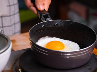 Close-up of frying tasty fried egg in a hot pan. Female hand breaks chicken egg falls into the kitchen pan. Concept of Nutritious Breakfast.
