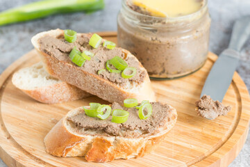 Homemade liver pate on fresh baguette, served on wooden cutting board