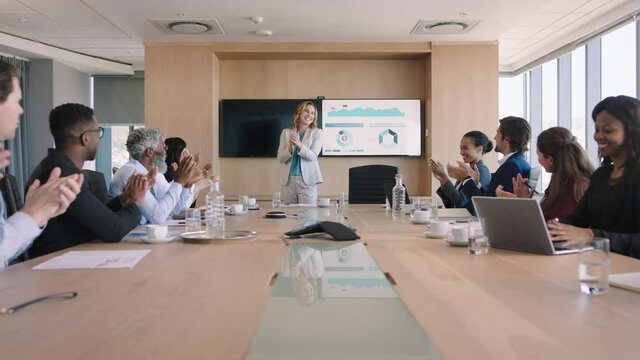 business people celebrating congratulating happy business woman presenting successful solution to shareholders clapping hands applause in office boardroom meeting