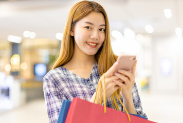 Smiling young Asian woman with shopping colour bags over mall background. using a smart phone shopping online  and smiling while standing mall building. lifestyle concept