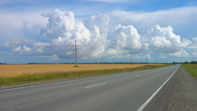 Automobile road against the background of picturesque clouds. The road diagonally goes into perspective, cars are passing along the road.
Against the background of golden grain fields.
