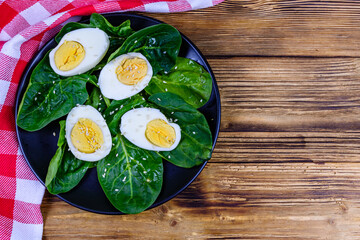 Spinach leaves and halved boiled eggs on a black plate. Top view