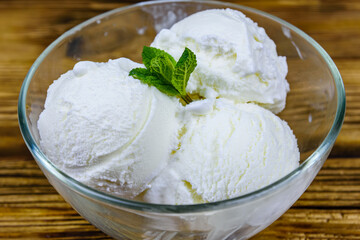 Glass bowl with ice cream balls and mint leaf on a wooden table