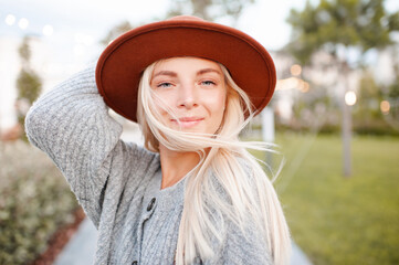 Beautiful blonde smiling adult girl 20-24 year old wear casual warm clothes and hat posing in city...