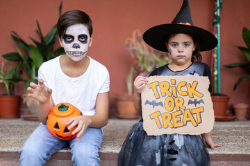 Boy and girl in typical Halloween costumes sitting at the entrance of their house.