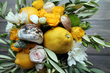 A bouquet of asters, yellow roses, real lemons, shells and olive leaves on a wooden background. The concept of gifts and congratulations for birthdays and various holidays. A pleasant surprise.