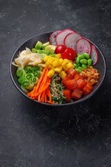 Hawaii salmon poke with vegetables with ginger, mango, cucumber and avocado, rice, seaweed, tomato. Asian salmon poke on dark stone background.