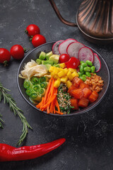 Hawaii salmon poke with vegetables with ginger, mango, cucumber and avocado, rice, seaweed, tomato. Asian salmon poke on dark stone background.