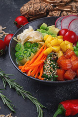 Hawaii salmon poke with vegetables with ginger, mango, cucumber and avocado, rice, seaweed, tomato. Asian salmon poke on dark stone background.