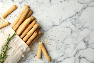 Delicious grissini sticks and rosemary on white marble table, flat lay. Space for text