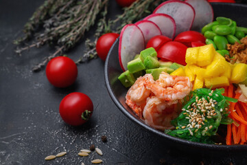Hawaii shrimp poke with vegetables with ginger, mango, cucumber and avocado, rice, seaweed, tomato. Asian salmon poke on dark stone background.