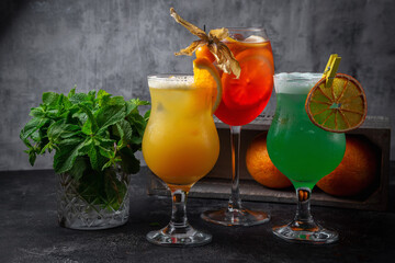 Alcoholic cocktails sangria, pina colada and mojito in glass glasses with citrus fruit, orange, lemon and mint on a dark background