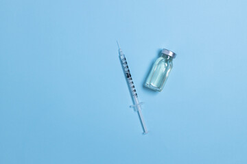 Vial with coronavirus vaccine and syringe on light blue background with copy space. Vaccination against influenza, covid 19, measles, coronavirus disease.