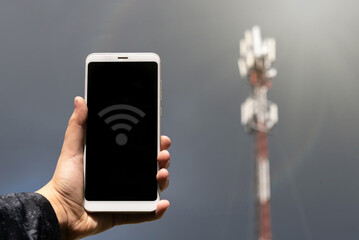 A hand holds a mobile phone on the background of a wireless communication station. High speed data transfer. Technologies