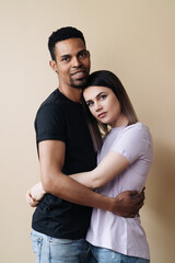 Portrait of happy multiracial couple hugging and posing together over beige background in studio, romantic guy cuddling his afro girlfriend