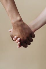 Multiethnic couple holding hands. Young Caucasian woman and African male arms together on beige background. Family Success concept