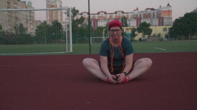 Plump caucasian woman stretching after training in the stadium. Overweight lady stretching on an outdoor sports ground. Sporty people lifestyle concept. ust keep calm and do sport.