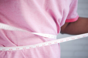 young man measuring his waist with a tape measure, close up.