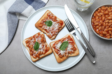 Toasts with delicious canned beans on light grey table, flat lay