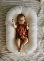 Three months old baby girl smiling, lying in a baby nest.