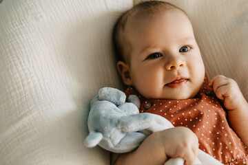 Closeup portrait of a three months old baby, smiling and hugging a plush toy.