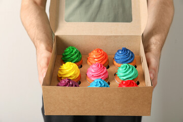 Man holding box with delicious colorful cupcakes on light background, closeup