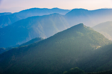 View of Himalayas mountain range with visible silhouettes through the colorful fog from Naina peak trek trail. Khalia top is at an altitude of 2615m himalayan region of Kumaon, Uttarakhand, India.